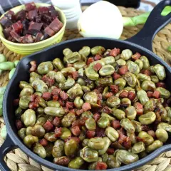 Habas tiernas salteadas con trocitos de jamón en una sartén de hierro fundido, un plato tradicional lleno de sabor.