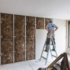Un ouvrier installe une isolation thermique pour éviter l'effet paroi froide. La structure métallique est remplie de laine minérale.