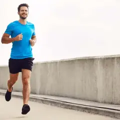 Lächelnder Mann joggt auf einer Straße, baut beim Joggen Muskeln auf.