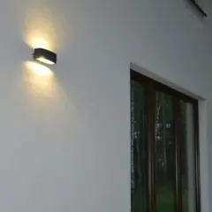 Nierówności na elewacji pod światło, tworzące ciekawe cienie. Dwa kinkietowe punkty świetlne oświetlają białą ścianę domu.