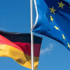 Die deutsche und die EU-Flagge wehen im Wind vor blauem Himmel.