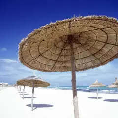 Słomiane parasole na białej plaży, idealne na upalną tunezyjską pogodę w sierpniu. Błękitne niebo i morze.