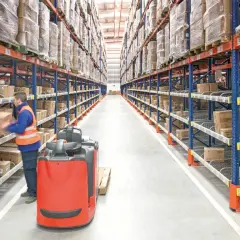 Pracownik magazynu, order picker, przenosi paczkę. Czy ciężko? Wysokie regały pełne towarów.