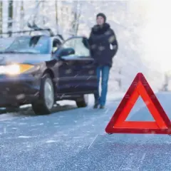 Gefährliche Straße: Ein Auto mit Warnblinker, eine Person und ein Warndreieck im Schnee. So entsteht Blitzeis.