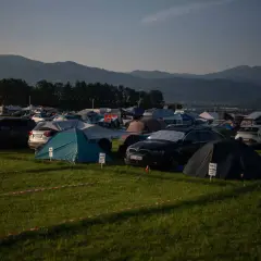 Rozległe pola namiotowe Austria, pełne namiotów i samochodów, z górami w tle.