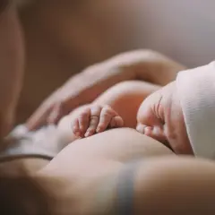 Delikatne dłonie noworodka obejmujące pierś podczas karmienia. Ulewanie u noworodka to częsty widok, ale ten moment to czysta bliskość.