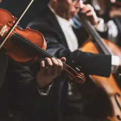 Muzycy w eleganckich strojach grają na instrumentach smyczkowych. W centrum uwagi skrzypek, a w tle wiolonczela. To piękny intro do koncertu.