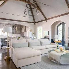 A spacious living room with a sectional sofa, armchair, and ottoman. The vaulted ceiling with exposed beams and a large chandelier create a dramatic focal point, showcasing what is the best way to arrange furniture for an open, airy feel.
