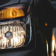 Luces cruce de un coche, con el intermitente naranja encendido y el faro principal iluminando. Otro coche se ve al fondo.