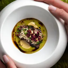 Wykwintne danie z restauracji z gwiazdką Michelin, podane w białej misie na tle mchu.