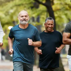 Quatre hommes d'âge mûr profitent d'une course matinale dans un parc, démontrant une excellente motricité adulte.