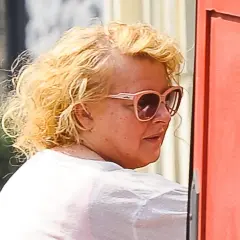 Magda Gessler bez peruki, w okularach przeciwsłonecznych, z kręconymi blond włosami, w białej koszulce.