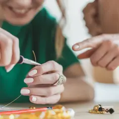 Dłonie tworzące biżuterię, używające szczypiec do drutu i koralików.