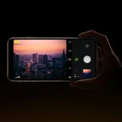 Dłoń trzyma smartfon z widokiem na miasto o zachodzie słońca. Na ekranie widać interfejs aparatu, gdzie można ustawić ISO.