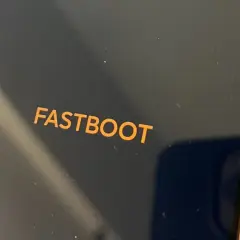 Pomarańczowy napis FASTBOOT na ciemnym ekranie telefonu, trzymanego w dłoni.