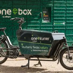 Rower cargo z napisem "one kurier by allegro" stoi przed zielonym paczkomatem "one box".