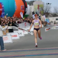 Radość na mecie Półmaratonu Warszawskiego 2026. Zawodniczka Glinka przekracza linię mety, a tłum wiwatuje.