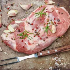Surowe mięso, czosnek, rozmaryn i kolorowe ziarna pieprzu na metalowej tacy. Widać piękny, różowy kolor mięsa po peklowaniu.