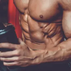 Atleta con addominali scolpiti prepara un frullato, mostrando a cosa servono le proteine in polvere palestra per la crescita muscolare.