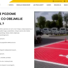 Malowanie oznaczenie miejsca dla niepełnosprawnych na czerwonym tle parkingu. W tle białe busy i drzewa.