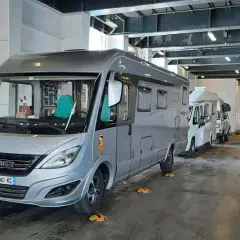 Camping-cars alignés dans la cale d'un ferry, prêts pour la traversée vers la Corse. Le tarif de la traversée pour la Corse en camping-car est affiché sur un panneau.