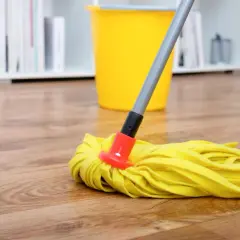 Ein gelber Wischmopp liegt auf einem Holzfußboden, bereit, den Boden zu wischen. Ein gelber Eimer steht im Hintergrund.