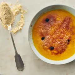 Ein Löffel mit feinem Puder liegt neben einer Schüssel mit karamellisiertem Creme Brulee.