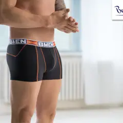 Mężczyzna w czarnych bokserkach z pomarańczowymi szwami i logo marki. Wybór między slipami a bokserkami to kwestia komfortu.