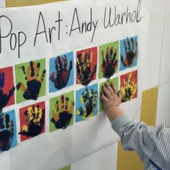 Manos pequeñas crean arte pop inspirado en Andy Warhol. Un niño toca una obra colorida, celebrando la creatividad infantil.