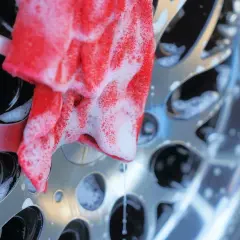Un chiffon rouge savonneux nettoie une jante de voiture brillante. Un nettoyant jantes maison efficace pour un résultat impeccable.