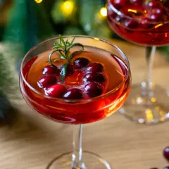 Festliche Aperol-Cocktails mit Cranberries und Rosmarin, perfekt für Aperol Weihnachten. Kleine Bäume und Lichter im Hintergrund.