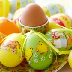 Un assortimento di colorate decorazioni uova di Pasqua con coniglietti, pulcini e fiori. Un uovo marrone è in un portauovo decorato.