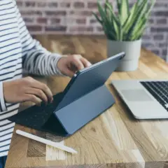 Osoba w paski pracuje na tablecie z klawiaturą, obok laptop. Może sprawdzać kursy walut w getin bank.