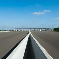 Péage autoroutier sous un ciel bleu. La route s'étend vers une barrière de péage avec plusieurs voies. Un camion jaune est visible.