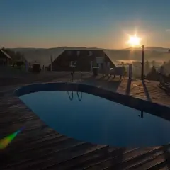 Poranek nad basenem z widokiem na Bieszczady. Słońce wschodzi nad mglistymi dolinami, tworząc magiczną atmosferę. Idealne miejsce na relaks w **termy Bieszczady**.