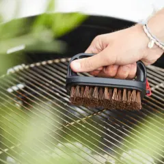 Maintenant, faut il huiler la grille du barbecue ? Une main nettoie la grille avec une brosse.