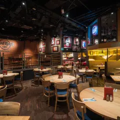 Wnętrze Hard Rock Cafe Warszawa. Drewniane stoły i krzesła, ściany ozdobione pamiątkami muzycznymi i neonem "Rock Radio".