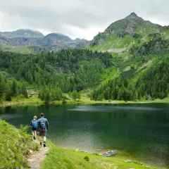 Para idąca ścieżką nad malowniczym jeziorem, otoczonym zielonymi wzgórzami i skalistymi szczytami. To piękne stawy w Tatrach.