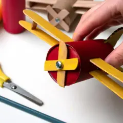 Un avión hecho con materiales de **avión manualidades**, sostenido por una mano. Tijeras y lápiz cerca, listos para crear más.
