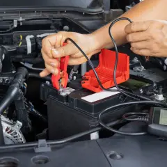 Ręce podłączają prostownik do akumulatora, by sprawdzić, czy można odpalić auto z prostownika.