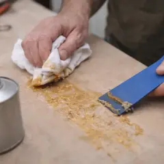 Comment enlever de la colle néoprène sur du tissu : un homme utilise une spatule bleue et un chiffon pour retirer la colle d'une surface.