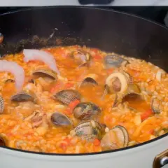 Un delicioso arroz a la marinera burbujea en una sartén, con gambas, almejas y calamares.