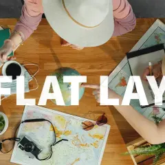 Widok z góry na stół z mapami, globusem, aparatem i notatkami. Dwie osoby planują podróż, tworząc inspirujący **flat lay**.