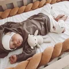 Słodki maluszek w brązowym dresie dla noworodka śpi w łóżeczku z pluszowym misiem.