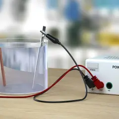 Eksperyment elektroliza wody: dwa elektrody w szklance z wodą, podłączone do zasilacza.
