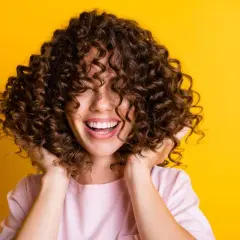 Mujer sonríe con cabello rizado y voluminoso. Descubre cómo hidratar el cabello después de una permanente para mantenerlo así de saludable.