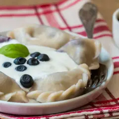 Pyszne pierogi z borówkami amerykańskimi, polane śmietaną i ozdobione świeżymi owocami. Idealne na letni deser.