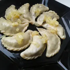 Pyszne pierogi z płuckami, polane skarmelizowaną cebulką, kuszą na czarnym talerzu.