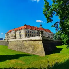 Zamek w Rzeszowie z czerwonym dachem i fosą otoczoną zielonym trawnikiem, pod błękitnym niebem.