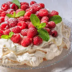 Beza Pavlova, która zawsze wychodzi, udekorowana świeżymi malinami i listkami mięty, posypana cukrem pudrem.
